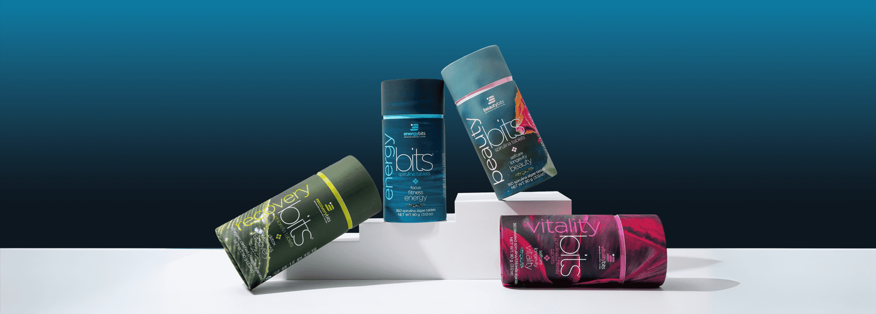 ENERGYbits product lineup—RECOVERYbits (chlorella), ENERGYbits & BEAUTYbits (spirulina), and VITALITYbits (50/50)—color canisters on white blocks against a dark teal gradient